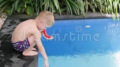 男孩在院子里的水池边吃西瓜。 小孩在度假时吃水果